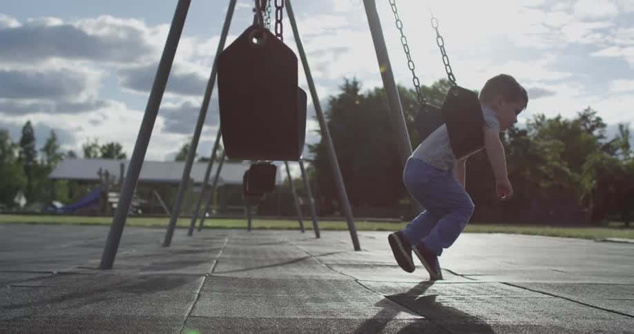 A boy walks over to a swing and rides it