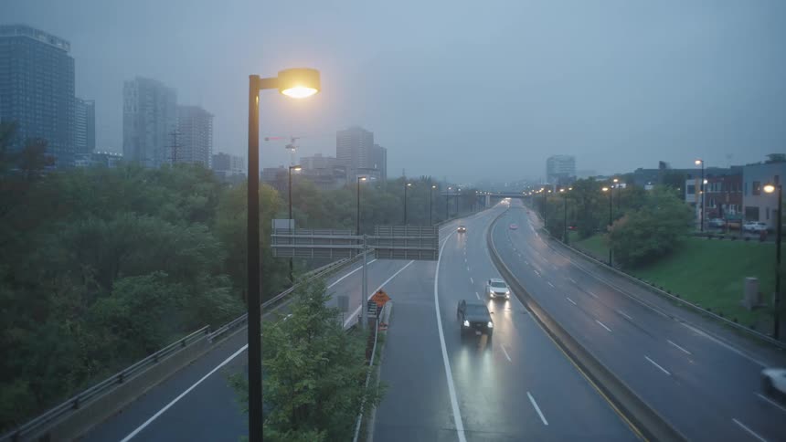 Vehicles drive along highway between apartment buildings and downtown skyscrapers on a foggy day