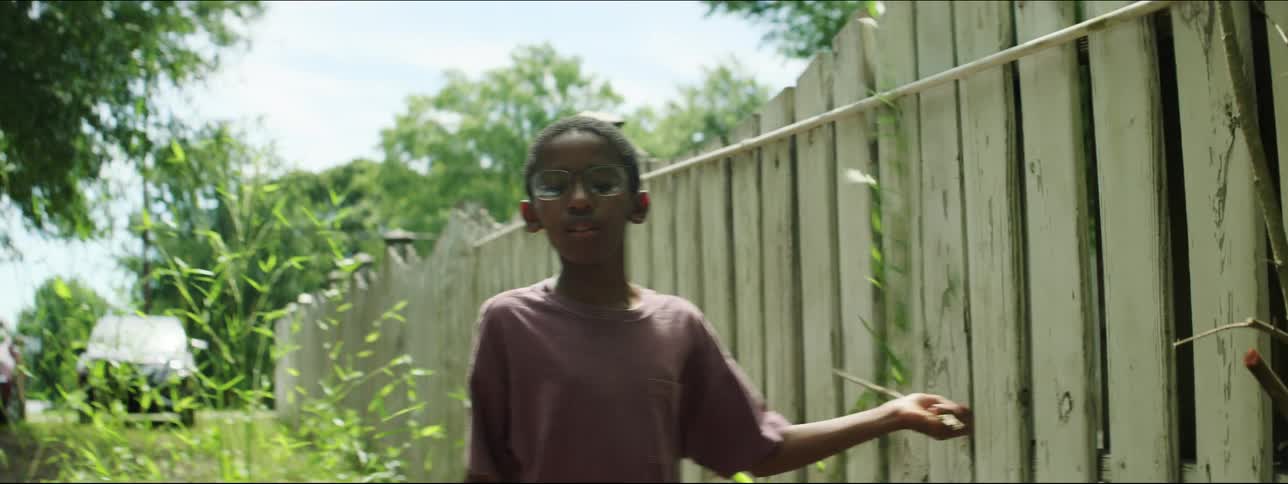 A child is walking past a fence with a stick