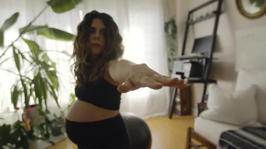 A pregnant woman practices yoga indoors during the day