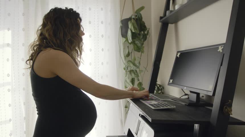Pregnant woman working out on a treadmill while working on a computer at home