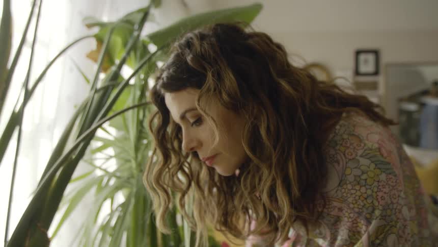 A woman in a room with plants a window a wall and a couch in the background