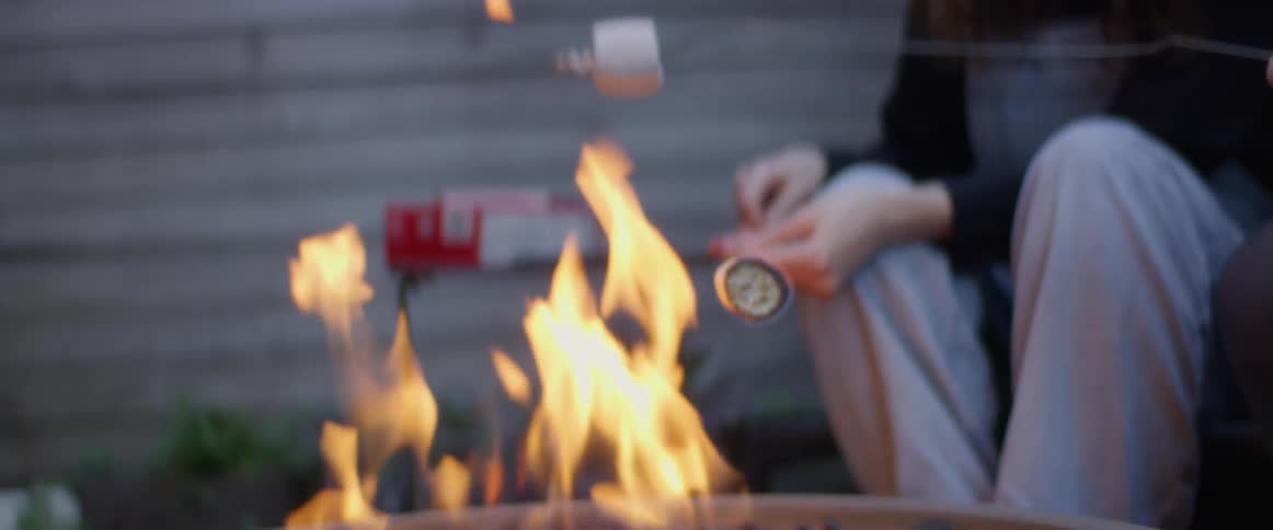 Friends sit outdoors around fire pit toasting marshmallows