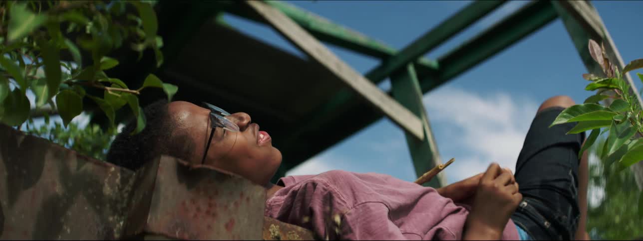 Youth lying on his back outdoors near metal structure laughs and talks