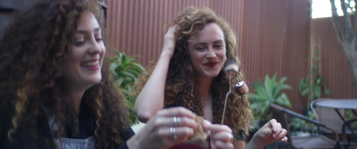 Friends sit outdoors laughing while toasting marshmallows as one opens package of crackers