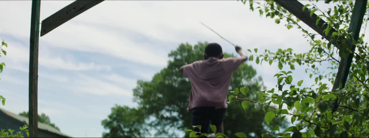 A young boy is holding a stick and jumps off a porch