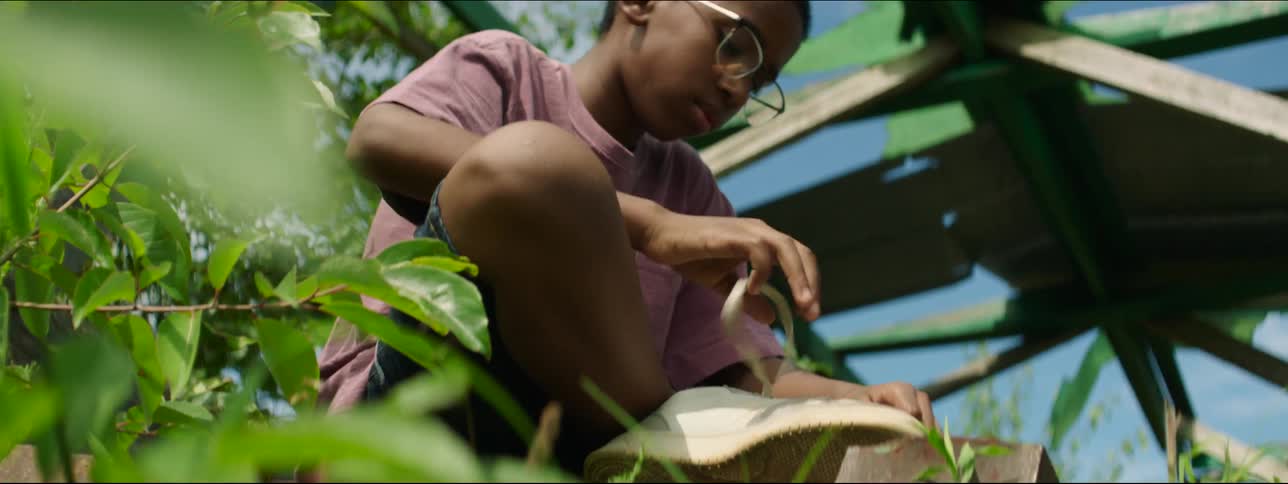 A boy with glasses tying the shoelace on his sneakers with the sky and clouds above