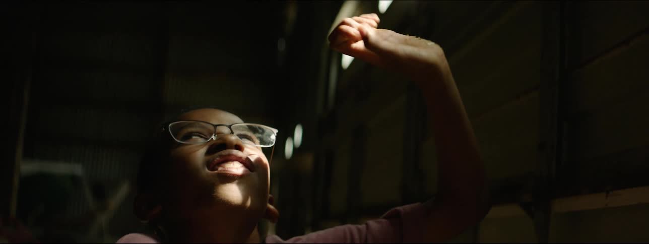 A boy in a dark barn looking at light beams in a door
