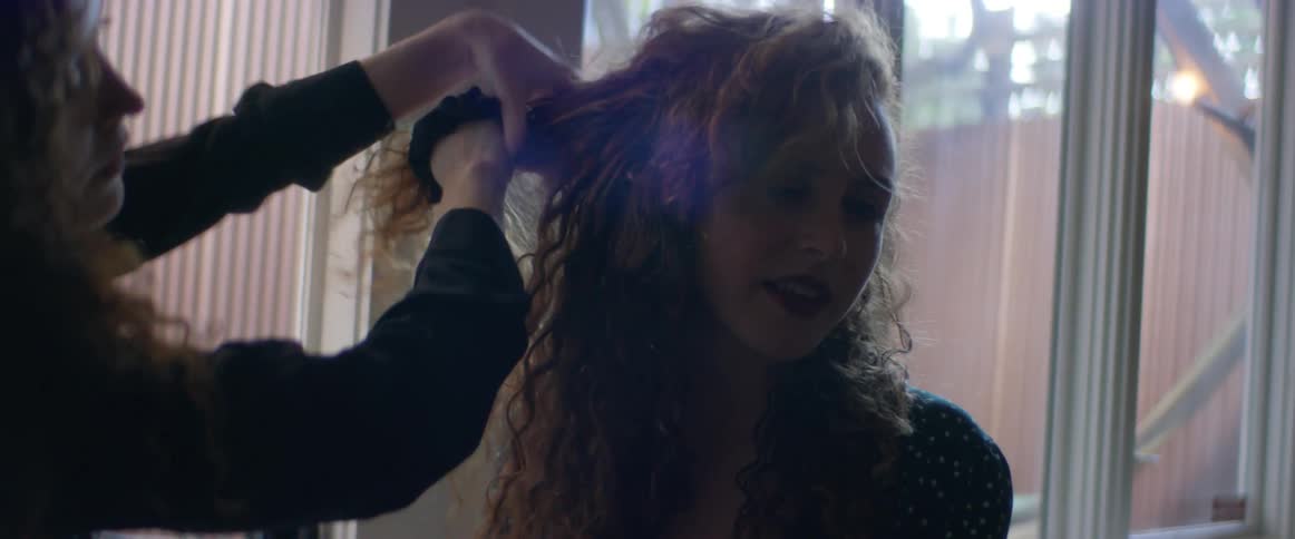 Two women are sitting together and one woman is fixing the other womans hair