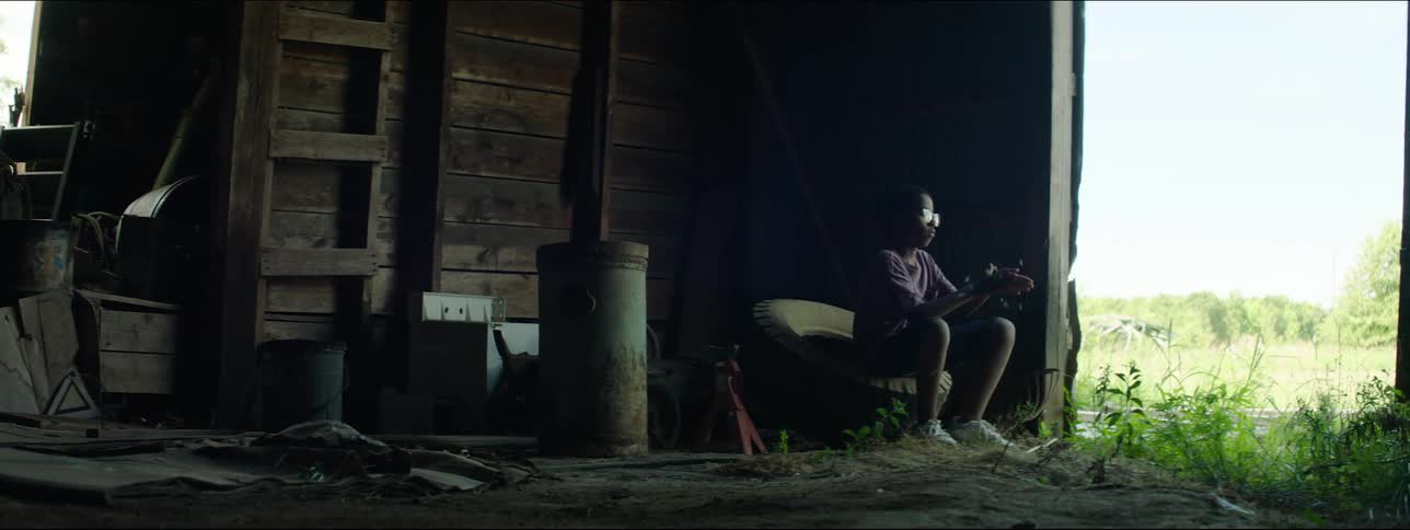 Boy sitting in barn blowing dandelion flower