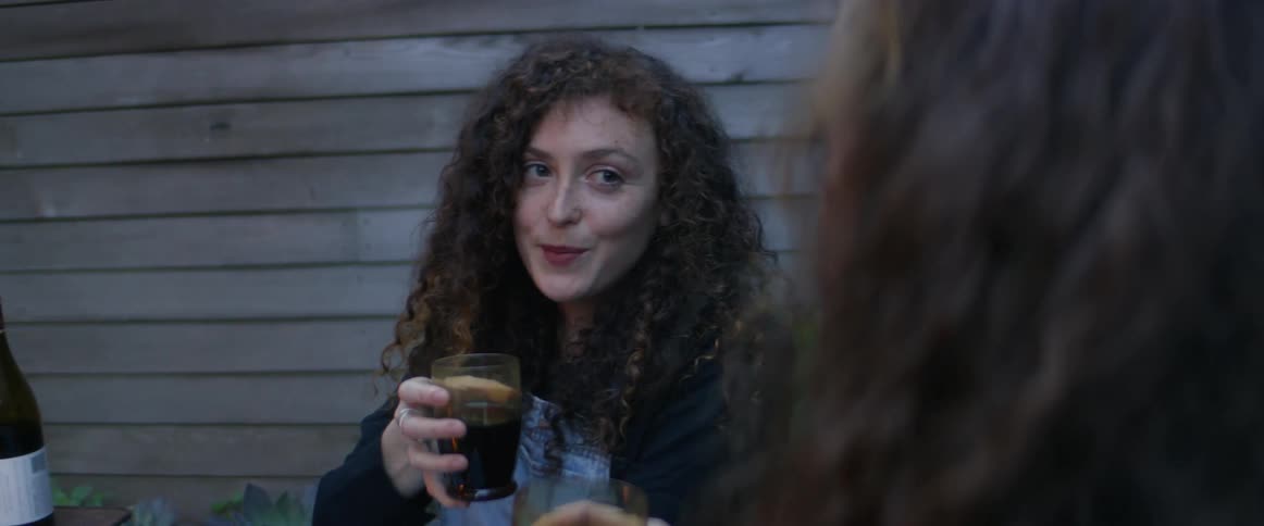 Two women sit outside and talk as they hold glasses of wine