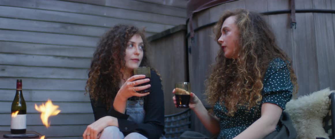 Two women drink wine by the fire