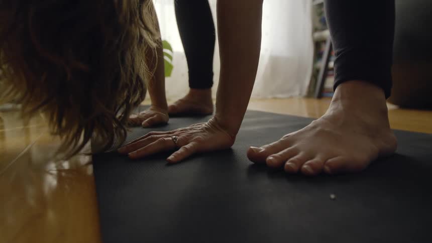 Pregnant woman with wavy hair and black leggings exercises on black fitness mat in living room at home