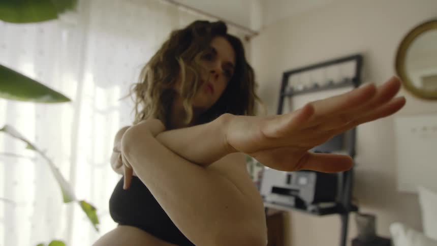 A pregnant woman is sitting in a chair doing stretching exercises in her bedroom during the day