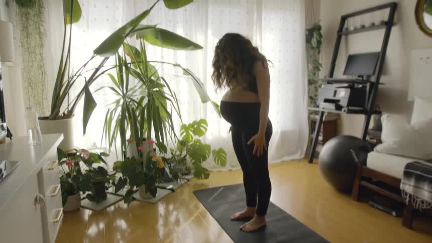 Woman with wavy hair black sports bra and leggings exercises on black fitness mat in the living room at home