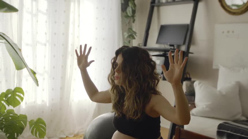 A pregnant woman is stretching and doing squats in her living room