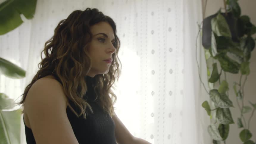 Woman with wavy hair exercises near window bordered by houseplants