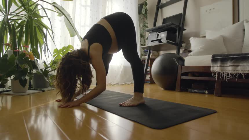A pregnant woman does stretches in the living room of a house during the day
