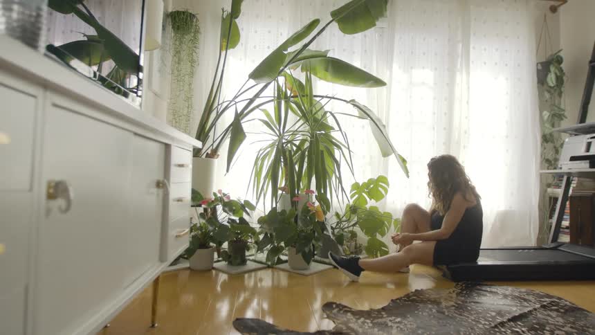A woman sits on a treadmill at home and ties her running shoes