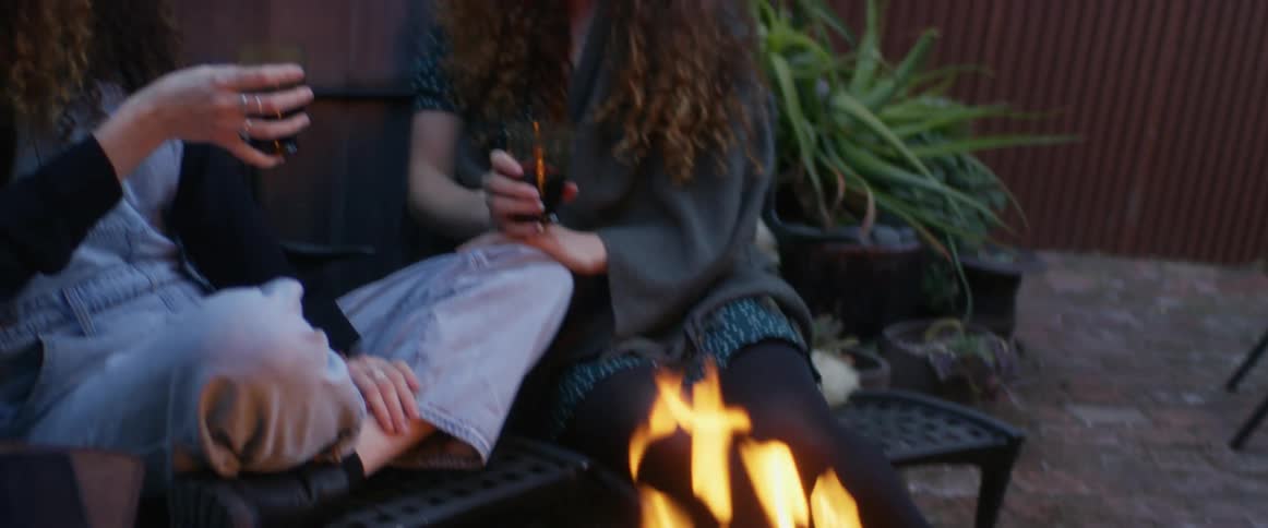 Two women drink by a fire pit in the yard