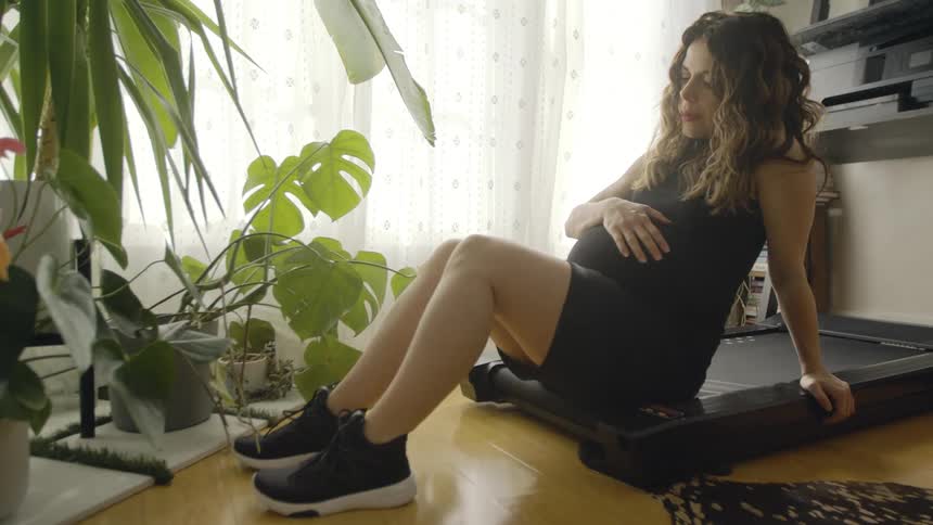 A pregnant woman sits at home and catches her breath and rubs her belly