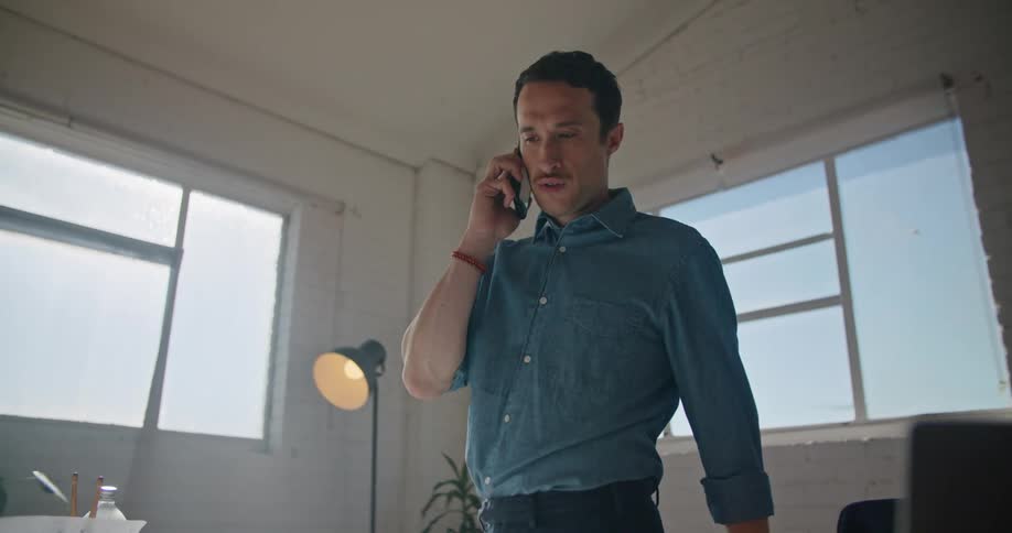 A man wearing a blue shirt is making a call on his cell phone
