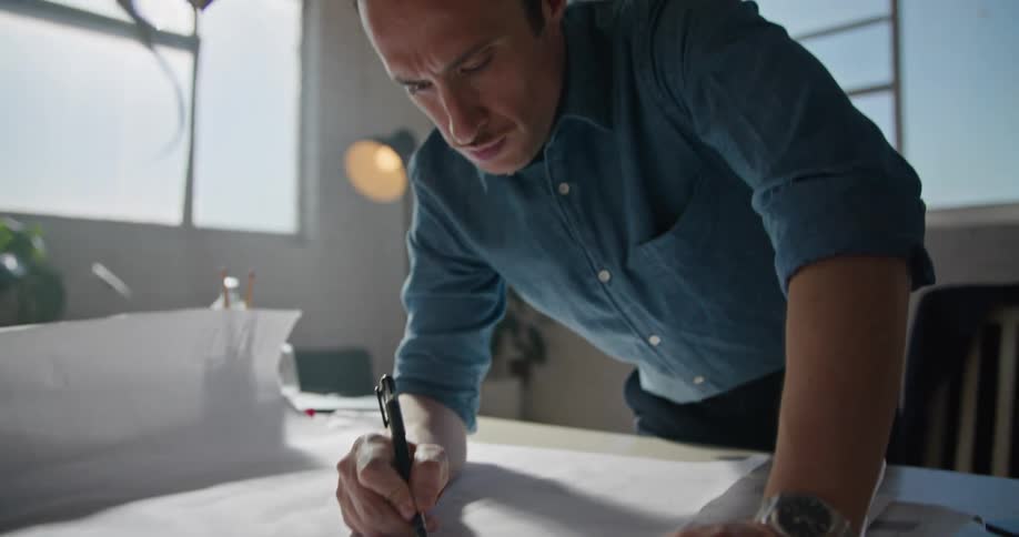 A man is leaning over a desk and drawing on a sheet of paper