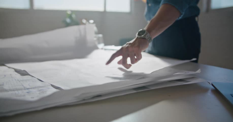A man in an office talks on a cell phone as he points at papers spread out on his desk