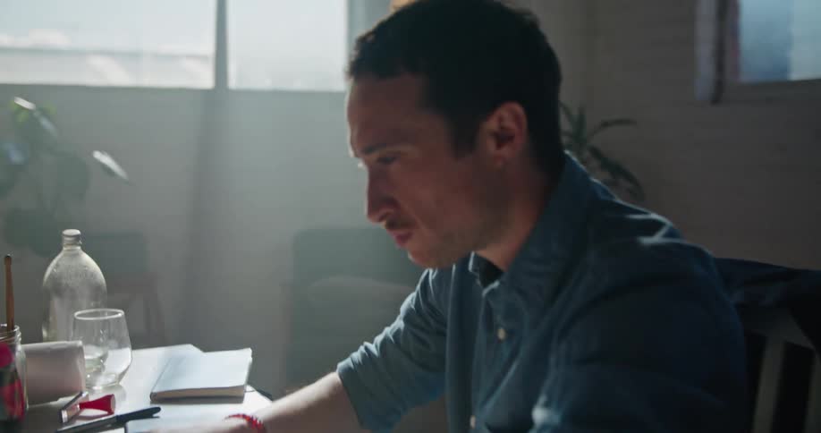 A man sitting at a desk stretches his arms out and starts typing on a laptop and then turns and winks