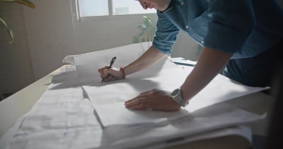 A man is talking on the phone in an office and making notes on blueprint paper during the daytime