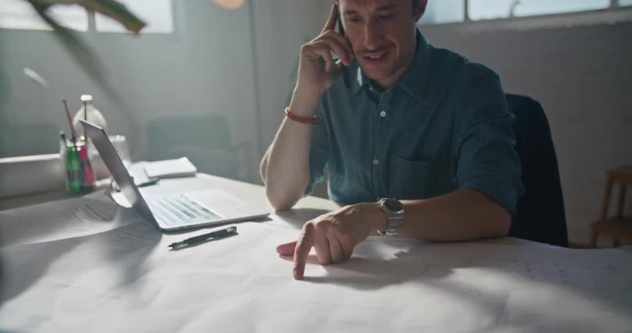 A man points at blueprints while talking on the phone