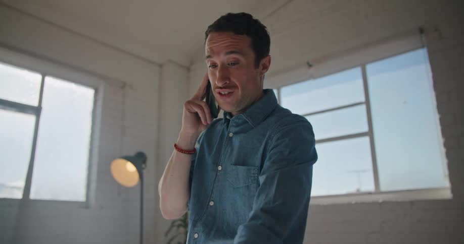 A man is talking on his cell phone while pointing at blueprints