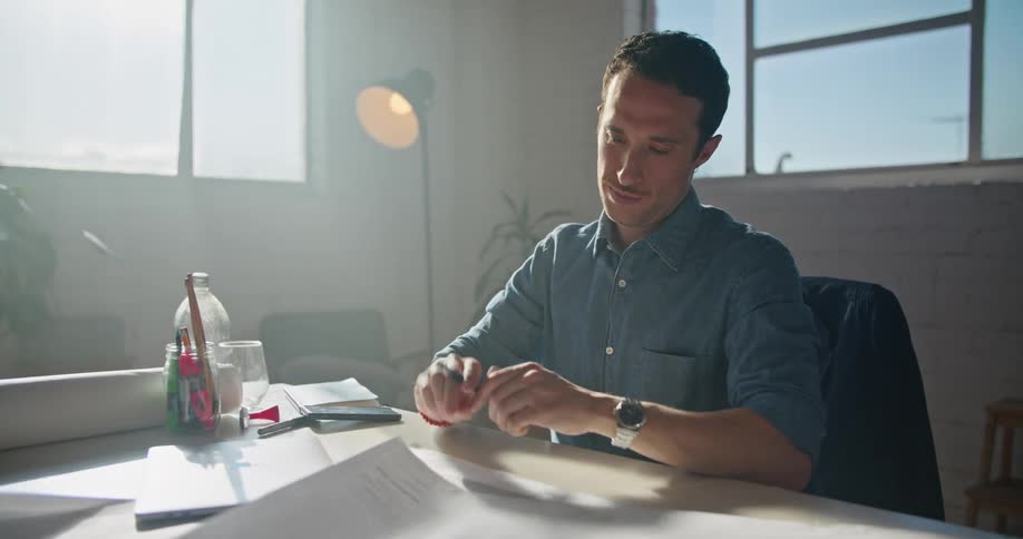 A man is sitting at a desk saying goodbye to someone on the computer and then he writes on paper on the desk