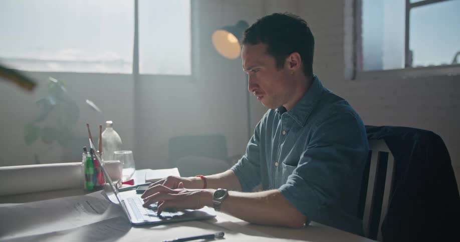 A man is typing on a laptop while seated in a home office during the day