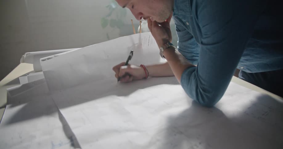 A man walks around an office talking on a cell phone and then goes to a desk and writes on paper