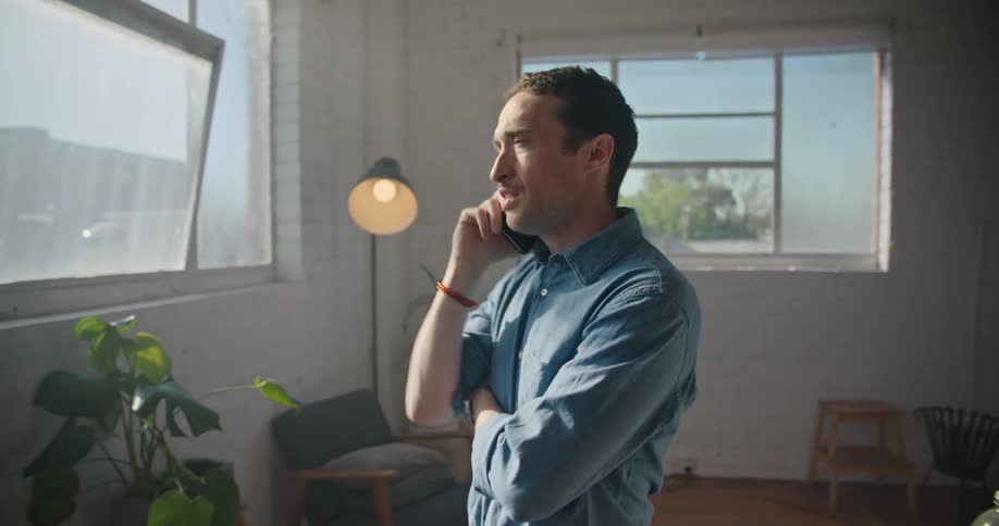 A man is walking around a room as he is talking on the phone and playing with a pen in his hand