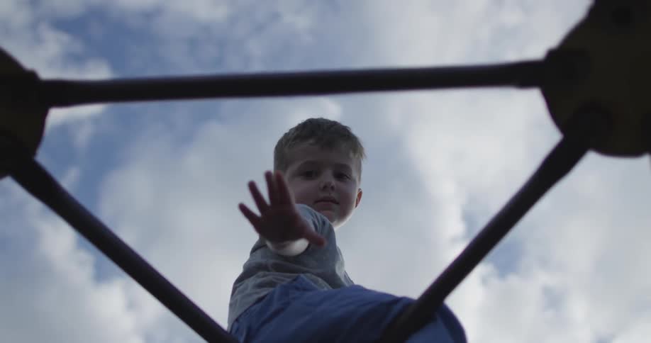 A boy reaches down from the top of a jungle gym