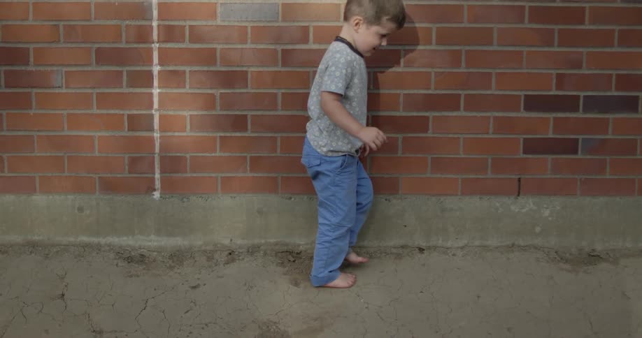A boy is walking barefoot near a brick wall