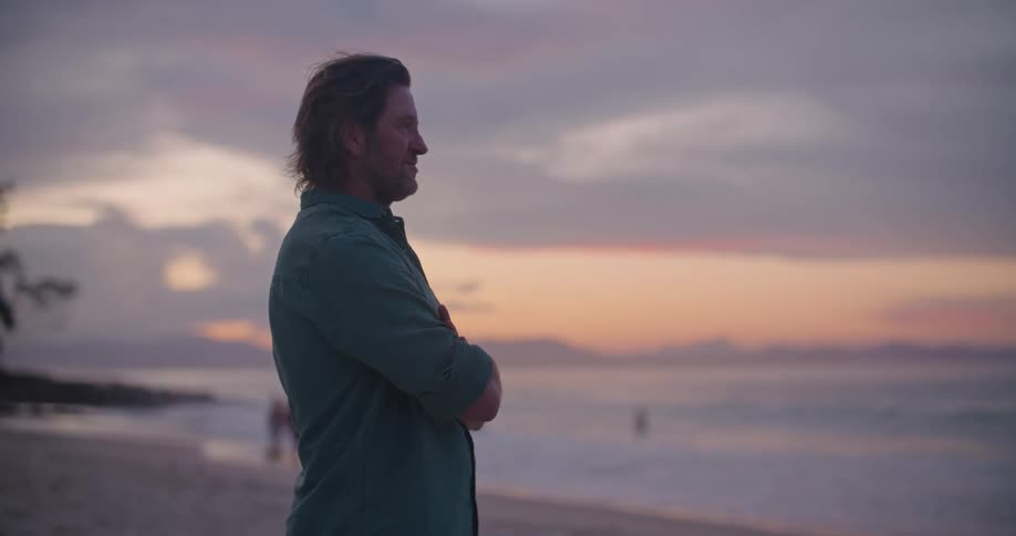 A man stands on the beach and watches people and surfing in the water