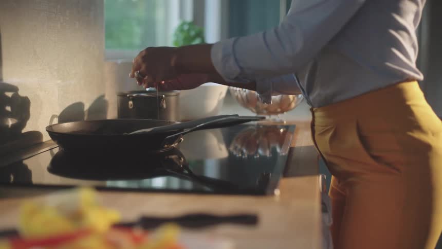 A woman is standing over a stove and cracking an egg into a frying pan