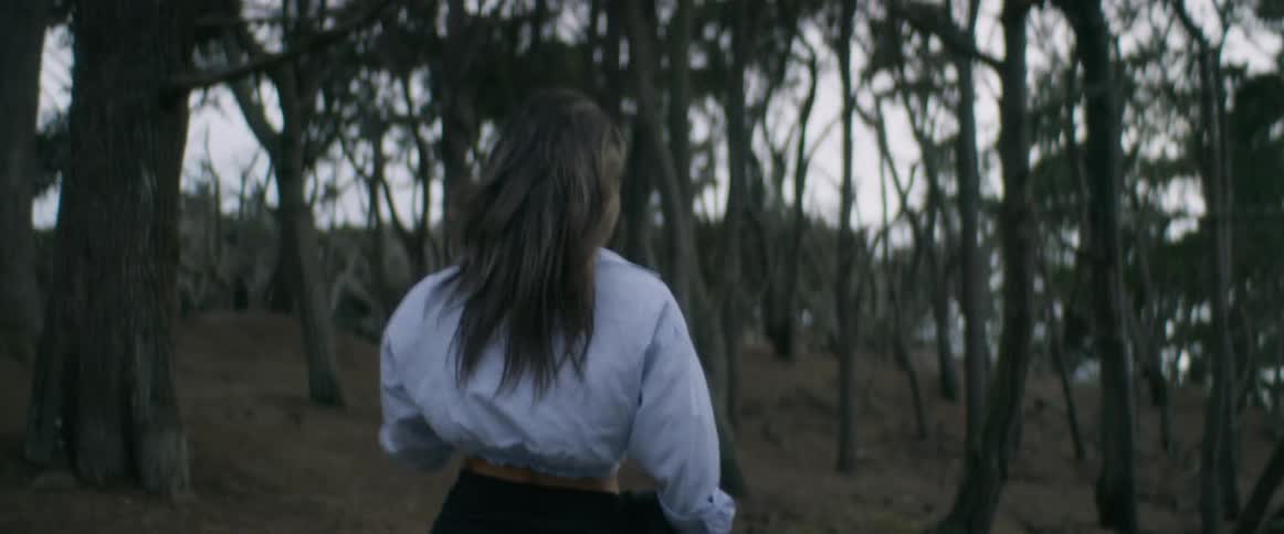 A woman with long hair is walking into an area with a lot of trees