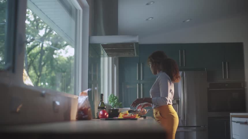 A woman cracks an egg while cooking in her kitchen