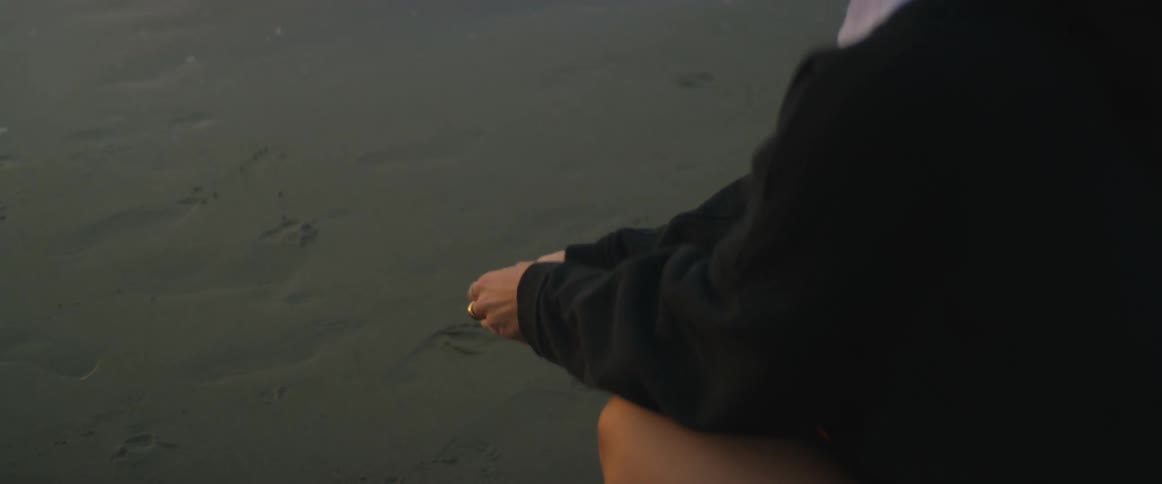 A woman with long dark hair is sitting on a beach watching the waves roll in