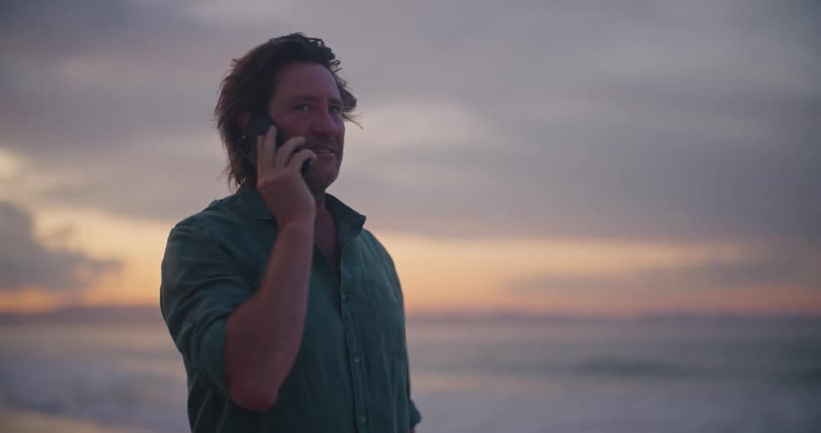 A man talks on the phone while standing on the beach