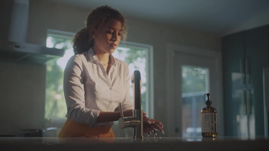 A woman is standing in front of a kitchen sink washing her hands