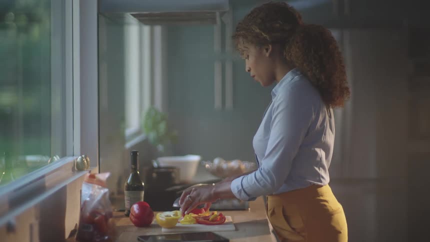 A woman cuts vegetables near a large window in her kitchen