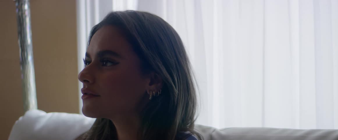 A woman sitting on a couch pushes her hair behind an ear