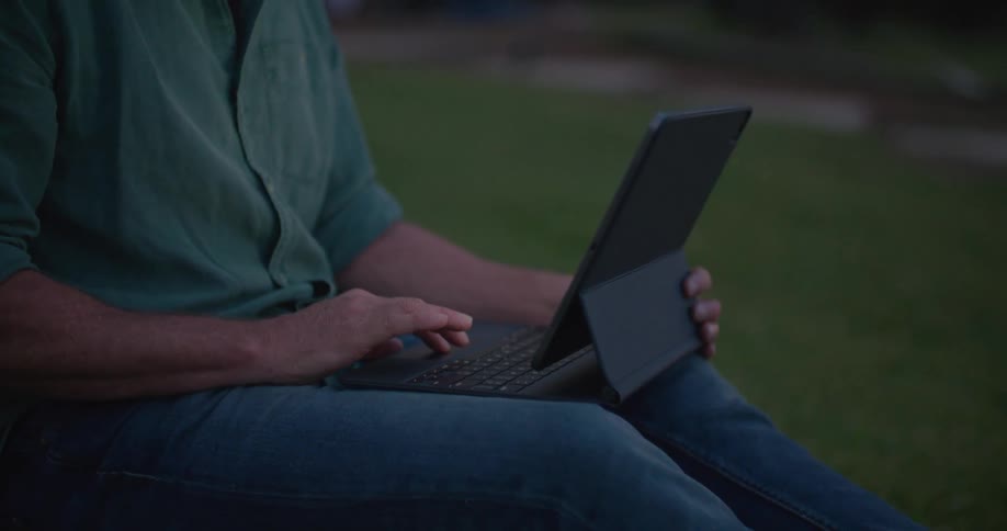 Mature man working on a laptop sitting outdoors at evening