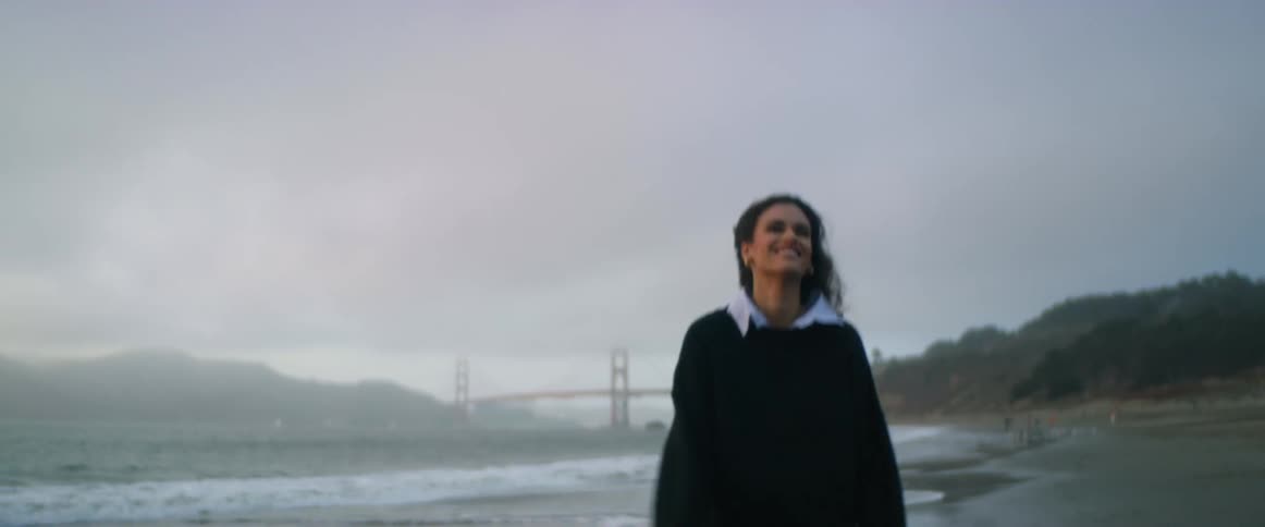 Young happy woman wearing black sweater walking on the beach near a bridge at evening