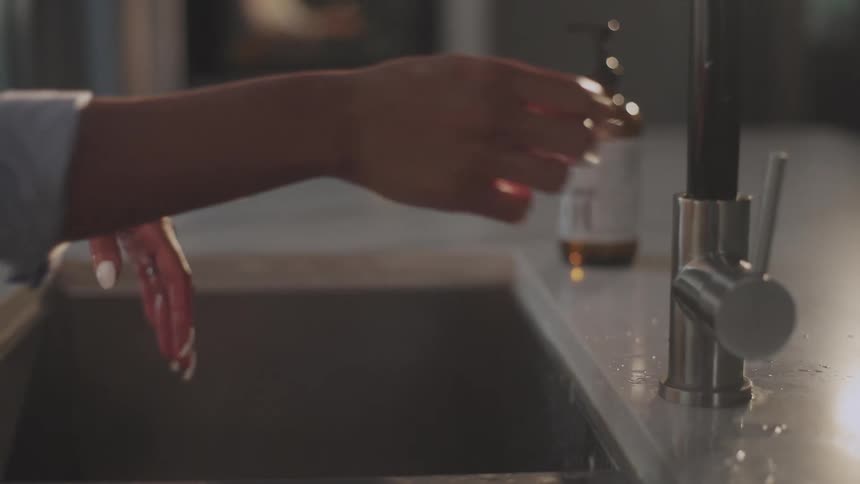 Woman with long white fingernails washes her hands on the kitchen sink